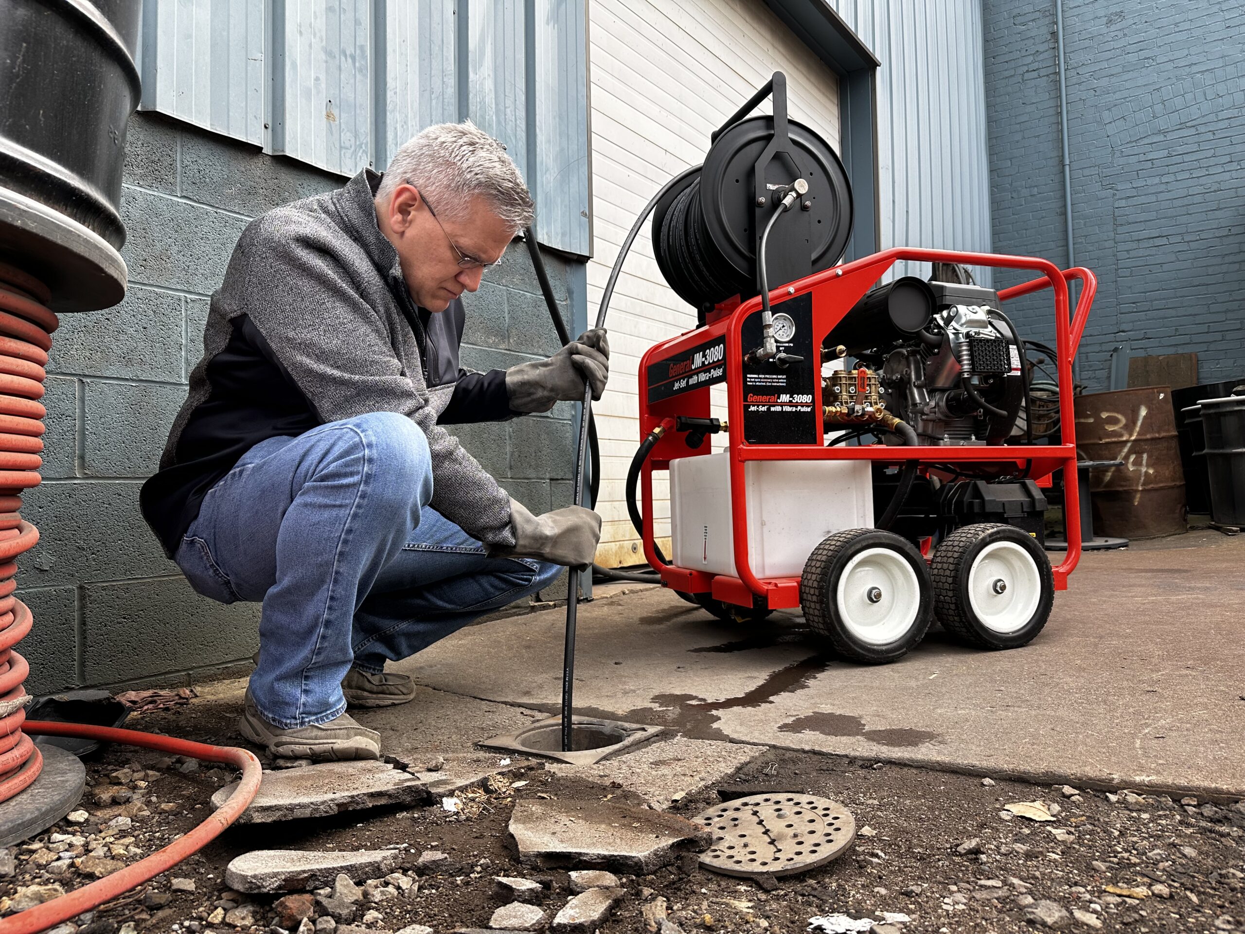 Plumber using hydro-jetting to clear main sewer line in yard